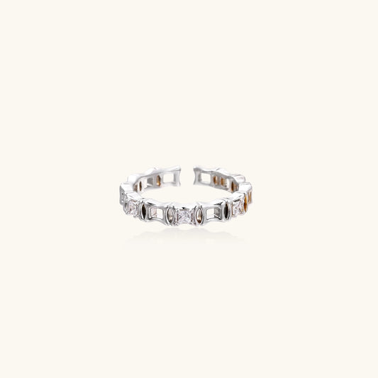 Close-up of geometric gold-plated ring with alternating rectangular blocks and zirconia crystals on white background.