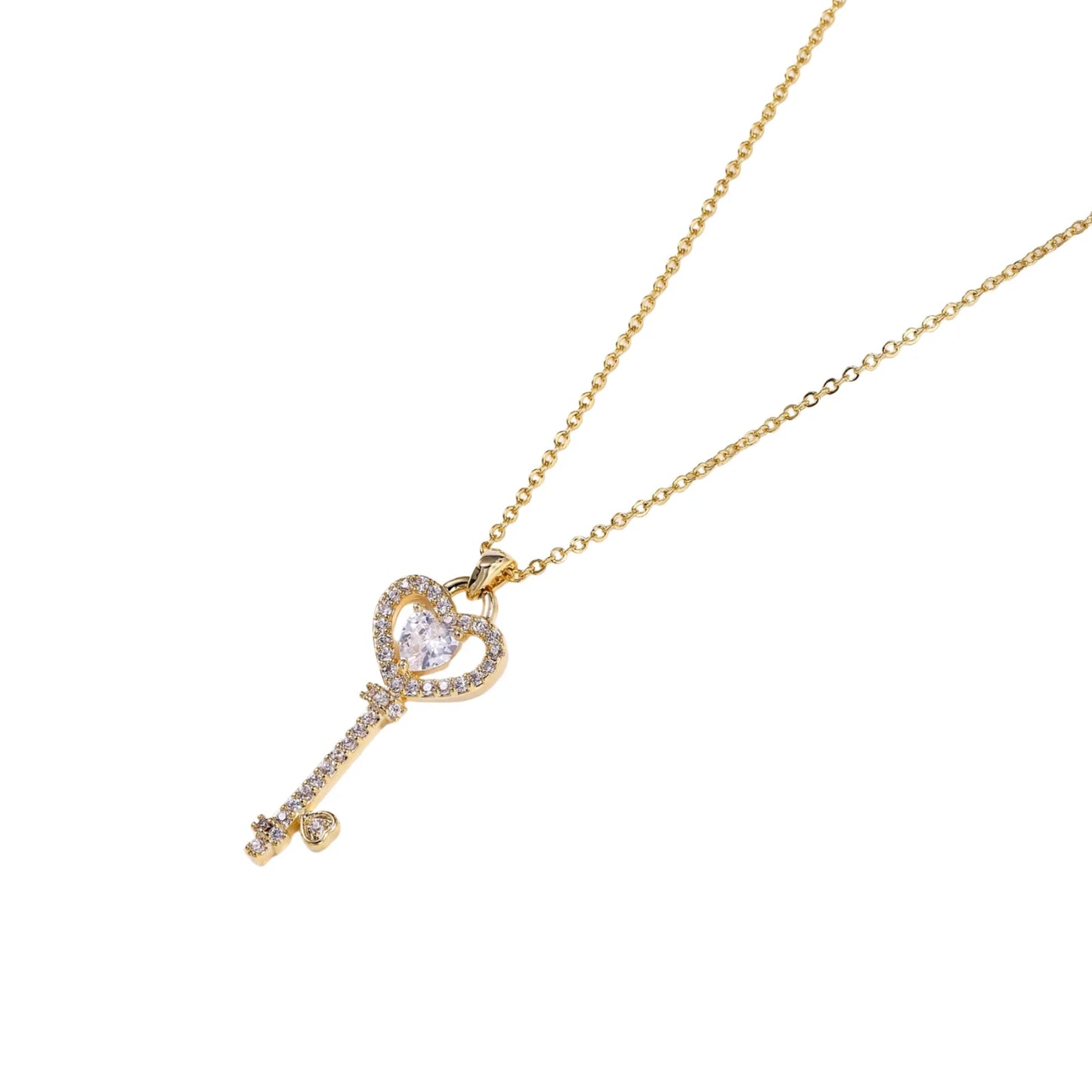 Delicate gold key pendant with heart-shaped bow and crystal pavé detailing on fine chain against cream background.