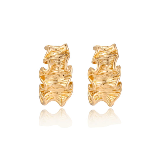 Pair of gold huggie hoops with sculpted wave texture and dimensional ripples on neutral background.