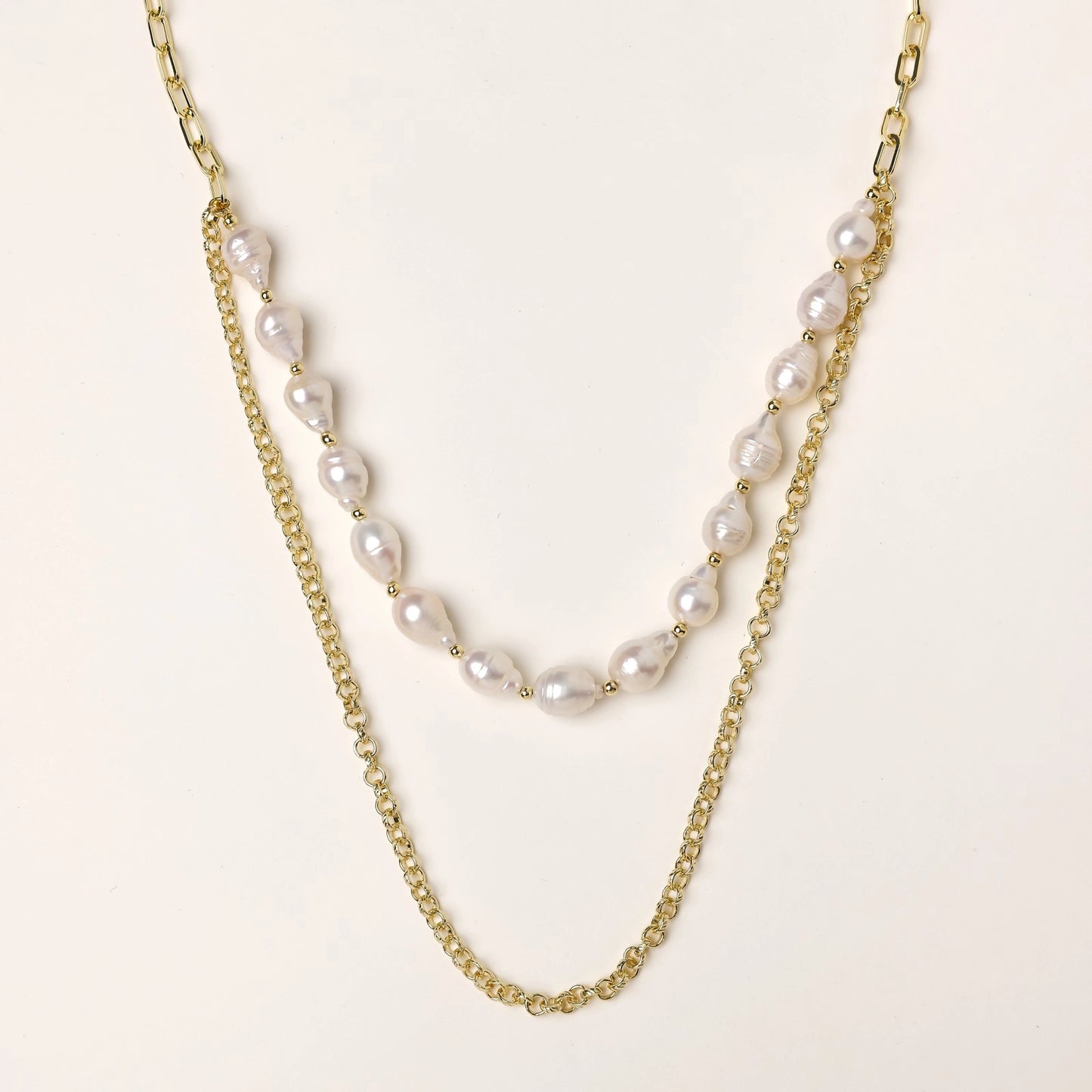Layered gold chain necklace with irregular freshwater pearls on cream background, showing adjustable dual-strand design.