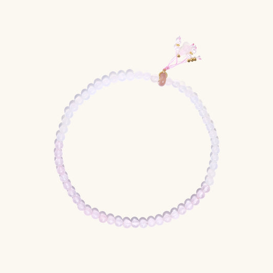 Stretchable bracelet with pink rose quartz and white agate beads, featuring a decorative tassel pendant on white background.