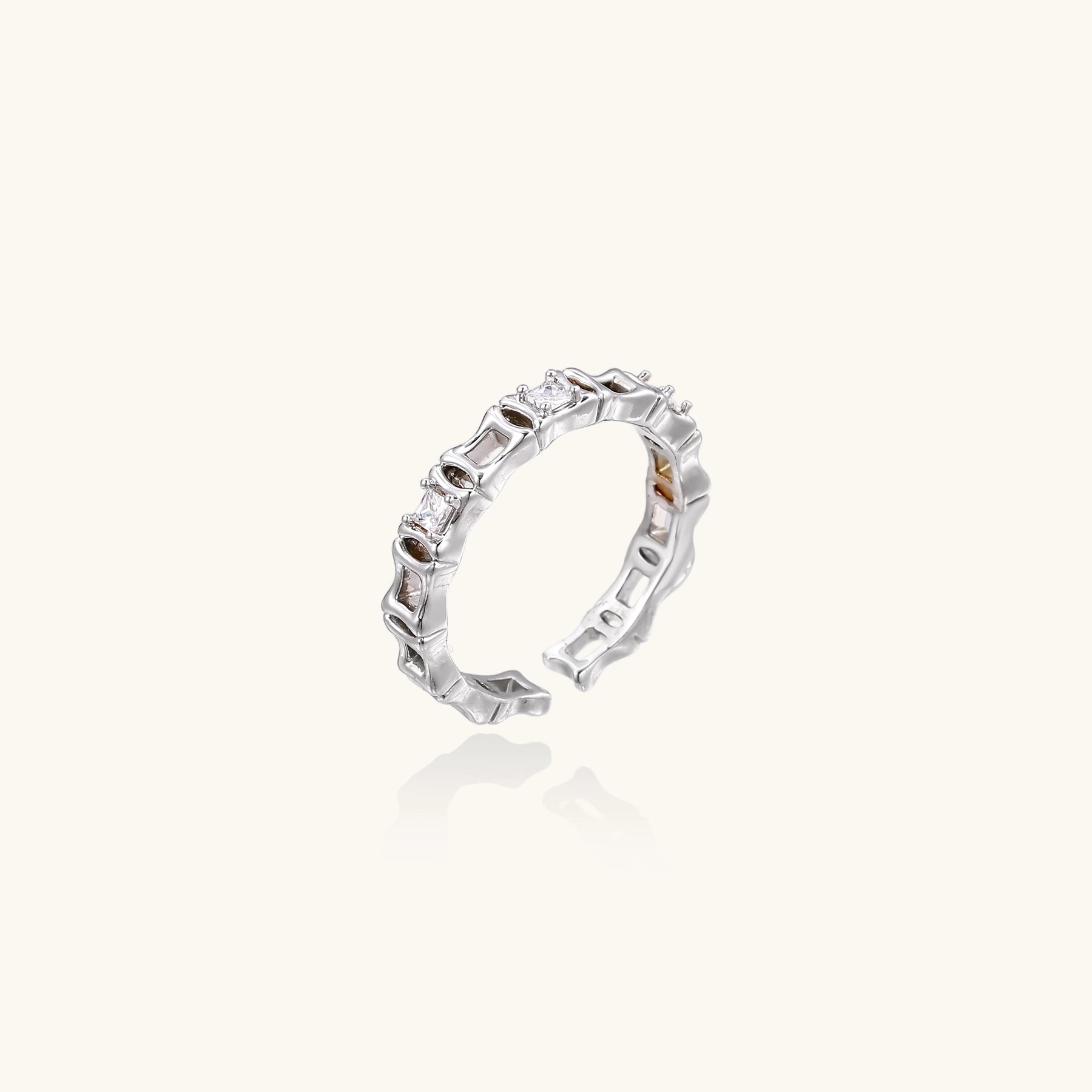 Close-up of geometric gold-plated ring with alternating rectangular blocks and zirconia crystals on white background.