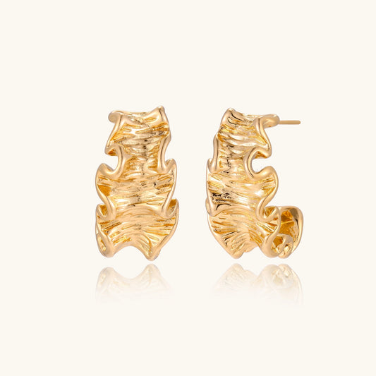 Close-up of dimensional gold-plated hoop earrings with rippled wave texture against white background.