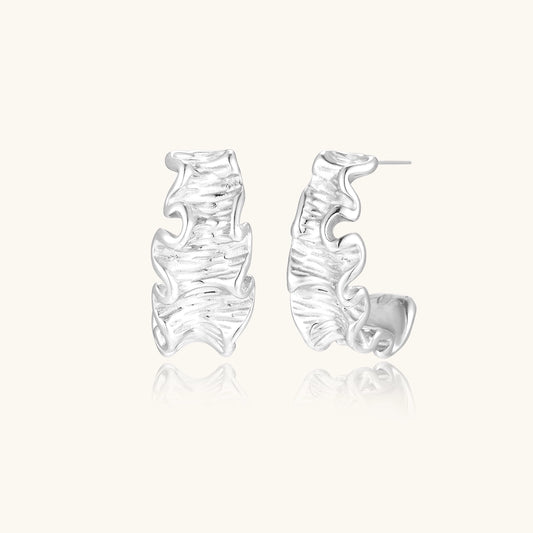 Textured gold-plated hoop earrings with flowing ripple design displayed on clean white background.