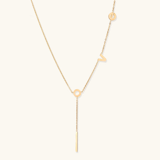 Gold-plated lariat necklace spelling LOVE with letter charms and vertical bar pendant on white background.