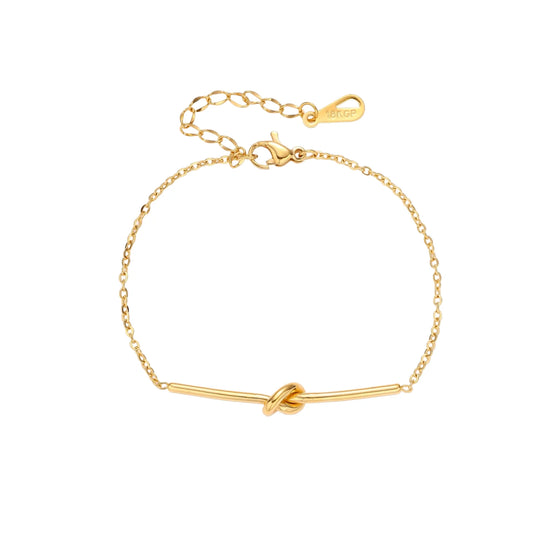 Delicate gold chain bracelet with minimalist bar and centered knot detail on cream background
